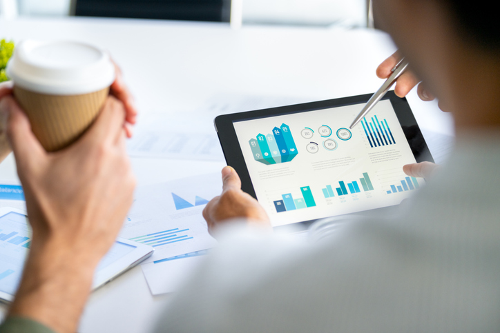 Three business men meeting and looking at financial data, charts and graphs on a digital tablet.